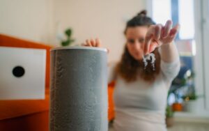 A person removes a clump of dust from an air purifier filter in a living room.