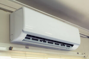 Wall-mounted air conditioning unit installed indoors, with vents open and positioned above a window.